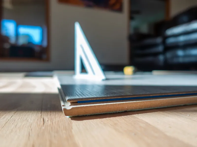 Close-up of engineered wood flooring layers showing wear layer thickness and parquet installation tools